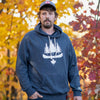 Adult male wearing a gray OBSC Heritage Hoodie with the logo visible on the front, standing outdoors with autumn leaves in the background.