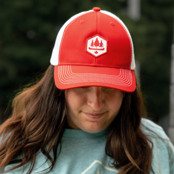 Woman wearing a red with white mesh backed hat, obsc logo, adjustable fit