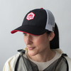 Woman wareing a black and white mesh backed hat with red accents, obsc logo, adjustable fit