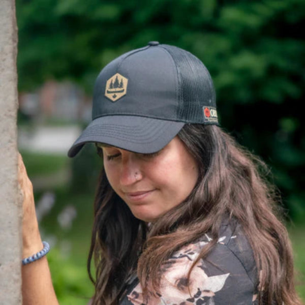 Woman wearing all black hat, with obsc logo, mesh back and adjustable 